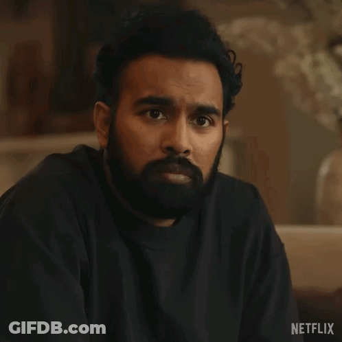 A Man With A Beard Is Sitting On A Couch With His Eyes Closed And A Black Shirt On . GIF
