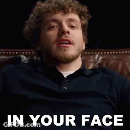 A Man With A Beard Is Sitting On A Couch With The Words In Your Face Behind Him GIF