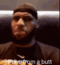 A Man With A Beard Is Sitting On A Couch With The Words Poop From A Butt Written On The Screen . GIF