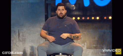 A Man With A Beard Is Sitting On A Stool In Front Of A Blue Sign That Says Vivavideo GIF