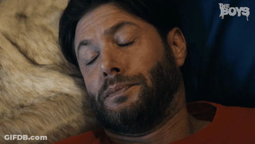 A Man With A Beard Is Sleeping In A Bed With The Boys Written In The Background GIF