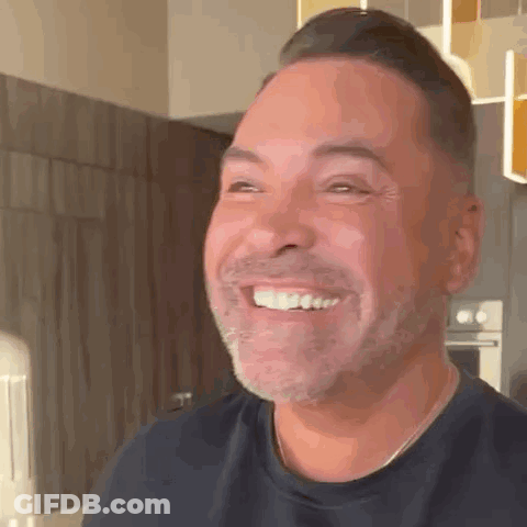 A Man With A Beard Is Smiling And Looking At The Camera . GIF