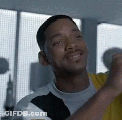 A Man With A Beard Is Smiling And Looking At The Camera While Standing In Front Of A Window . GIF