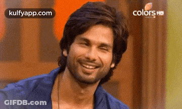 A Man With A Beard Is Smiling And Looking At The Camera While Wearing A Blue Shirt . GIF