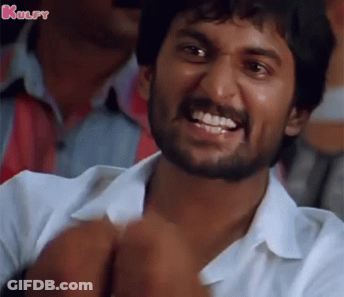 A Man With A Beard Is Smiling And Making A Funny Face While Sitting In A Crowd . GIF