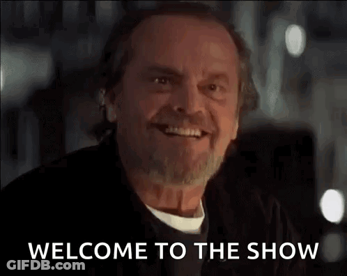 A Man With A Beard Is Smiling And Saying Welcome To The Show GIF