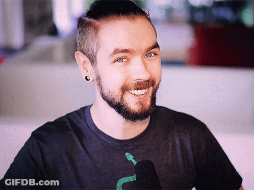A Man With A Beard Is Smiling And Wearing A Black Shirt With A Snake On It GIF