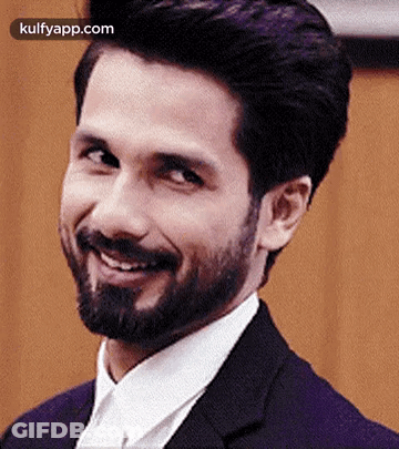 A Man With A Beard Is Smiling For The Camera While Wearing A Suit And Tie . GIF