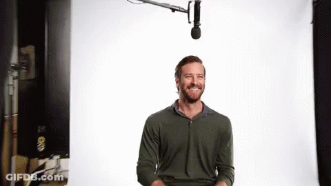 A Man With A Beard Is Smiling In Front Of A Microphone In A Studio . GIF