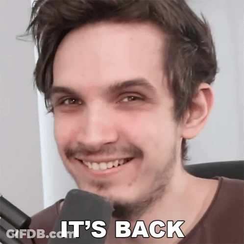 A Man With A Beard Is Smiling In Front Of A Microphone With The Words " It 'S Back " Written Below Him GIF