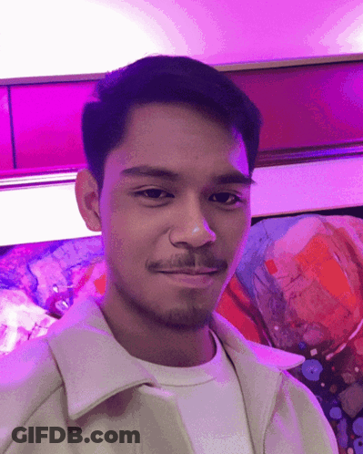 A Man With A Beard Is Smiling In Front Of A Painting GIF
