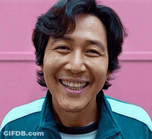 A Man With A Beard Is Smiling In Front Of A Pink Wall . GIF