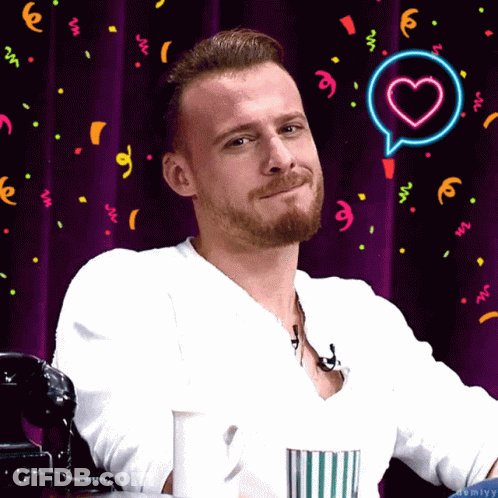 A Man With A Beard Is Smiling In Front Of A Purple Curtain GIF