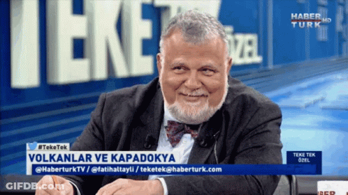 A Man With A Beard Is Smiling In Front Of A Sign That Says " Haber Turk " GIF