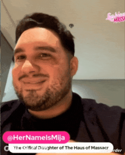 A Man With A Beard Is Smiling In Front Of A Sign That Says " The Official Daughter Of The Haus Of Massacr " GIF
