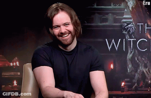 A Man With A Beard Is Smiling In Front Of A Sign That Says The Witch GIF