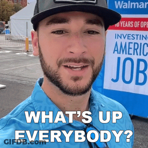 A Man With A Beard Is Smiling In Front Of A Sign That Says What 'S Up Everybody GIF
