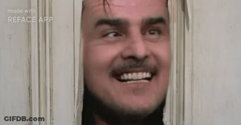 A Man With A Beard Is Smiling While Looking Through A Door . GIF