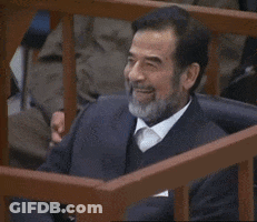 A Man With A Beard Is Smiling While Sitting Behind A Wooden Fence GIF