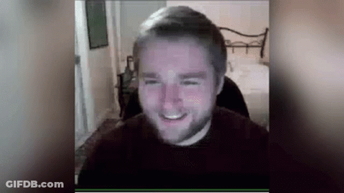 A Man With A Beard Is Smiling While Sitting In Front Of A Computer Monitor . GIF