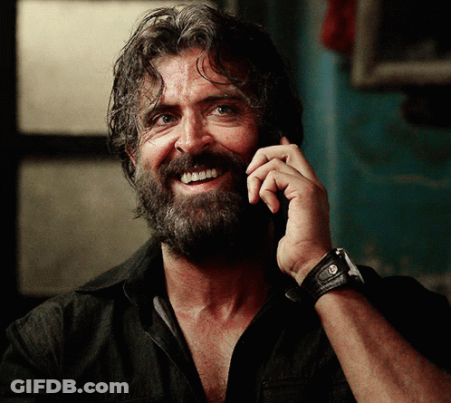 A Man With A Beard Is Smiling While Talking On A Phone GIF