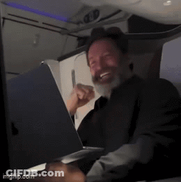 A Man With A Beard Is Smiling While Using A Laptop GIF