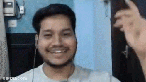 A Man With A Beard Is Smiling While Wearing Headphones And A White Shirt . GIF