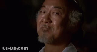 A Man With A Beard Is Smiling With His Eyes Closed While Sitting In A Dark Room . GIF