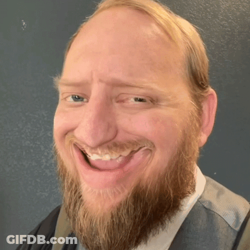 A Man With A Beard Is Smiling With His Tongue Sticking Out GIF
