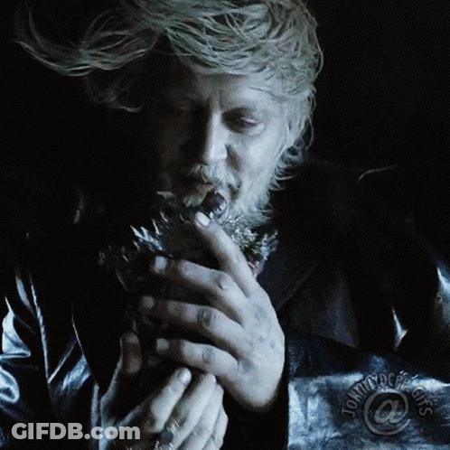 A Man With A Beard Is Smoking A Cigarette In A Dark Room With Tommy Doe 'S Logo On The Bottom Right GIF