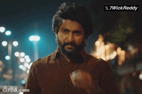 A Man With A Beard Is Smoking A Cigarette In Front Of A Sign That Says X7wick Reddy GIF