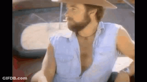 A Man With A Beard Is Smoking A Cigarette While Wearing A Cowboy Hat . GIF