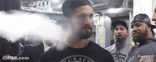 A Man With A Beard Is Smoking An Electronic Cigarette In Front Of A Group Of People . GIF