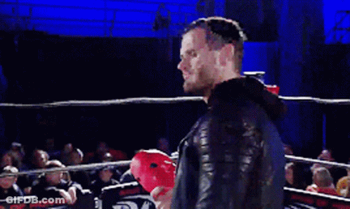 A Man With A Beard Is Speaking Into A Microphone In Front Of A Crowd Of People GIF