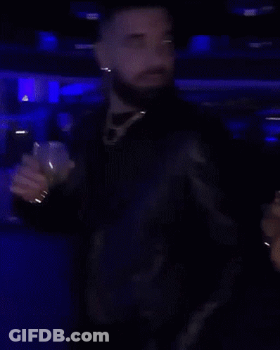 A Man With A Beard Is Standing In A Dark Room Holding A Glass GIF