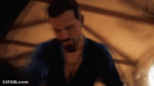 A Man With A Beard Is Standing In A Dark Room In A Dark Room . GIF