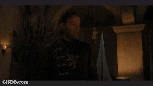 A Man With A Beard Is Standing In A Dark Room In Front Of A Fireplace GIF