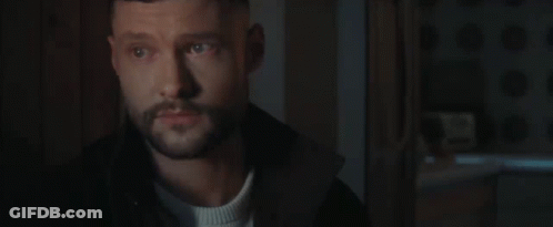 A Man With A Beard Is Standing In A Dark Room Looking At Something . GIF