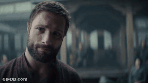 A Man With A Beard Is Standing In A Dark Room Looking At The Camera . GIF