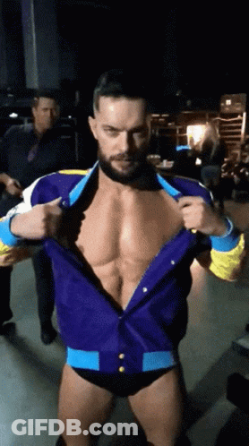 A Man With A Beard Is Standing In A Dark Room Taking Off His Shirt GIF