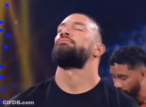 A Man With A Beard Is Standing In A Dark Room With His Eyes Closed And His Mouth Open . GIF