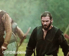A Man With A Beard Is Standing In A Field Looking At Something GIF