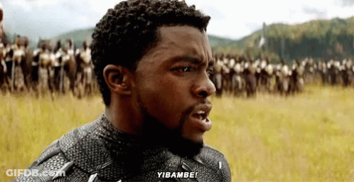 A Man With A Beard Is Standing In A Field With A Crowd Of People Behind Him And Says Yibambo ! GIF
