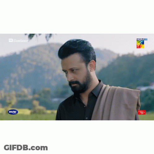 A Man With A Beard Is Standing In A Field With Mountains In The Background And A Advertisement For Itel On The Bottom Ri GIF