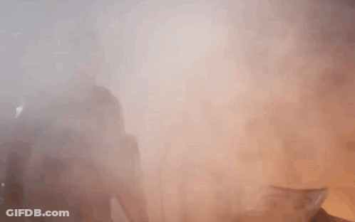 A Man With A Beard Is Standing In A Foggy Room With His Hands Outstretched . GIF