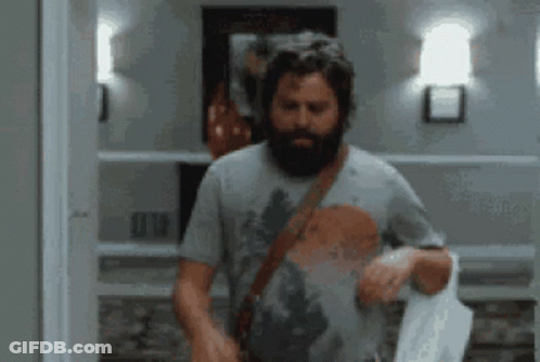 A Man With A Beard Is Standing In A Hallway Holding A Towel GIF