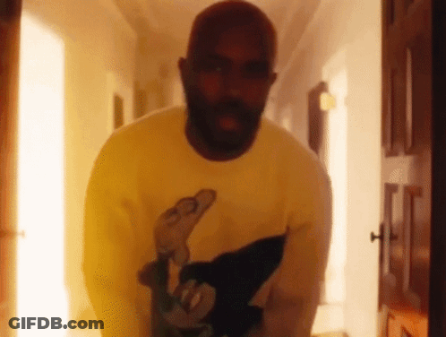 A Man With A Beard Is Standing In A Hallway Wearing A Yellow Sweater . GIF
