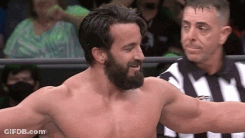 A Man With A Beard Is Standing In A Ring With A Referee . GIF