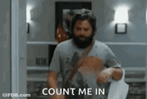 A Man With A Beard Is Standing In A Room Holding A Piece Of Paper . GIF
