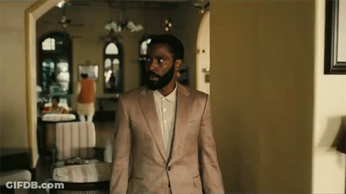 A Man With A Beard Is Standing In A Room Wearing A Pink Suit And White Shirt . GIF